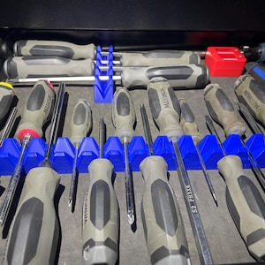 Op de afbeelding: Een close-up van een lade-organizer met een verscheidenheid aan schroevendraaiers. De organizer is gemaakt van blauw plastic en heeft slots voor elke schroevendraaier. De schroevendraaiers zijn allemaal van verschillende groottes en hebben zwarte en grijze handvatten.