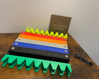 May include: A set of six colorful 3D printed blocks with the text "3D CONCEPTS CANADA" on each block. The blocks are stacked on top of each other and are arranged in a staggered pattern. The blocks are made of a smooth, glossy plastic. The blocks are a bright yellow, orange, red, light gray, blue, and black.