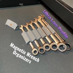 Puede incluir: Un juego de llaves de color dorado con organizadores magnéticos grises. Las llaves están dispuestas sobre una superficie gris oscuro. El texto de la imagen dice "Magnetic Wrench Organizers" y "Ultra Low-Profile".