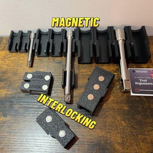 Puede incluir: Organizadores de herramientas magnéticos negros y soportes magnéticos entrelazados. La imagen muestra varios soportes de plástico negro, herramientas de metal y pequeños soportes negros con imanes. Se muestra el texto "MAGNETIC" e "INTERLOCKING".