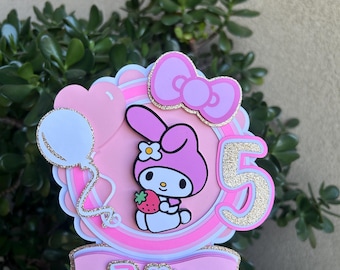 May include: A pink and white cake topper featuring a cartoon character holding a strawberry. The topper includes a bow, balloons, the number 5, and the name "Zellie". The design has glitter accents.