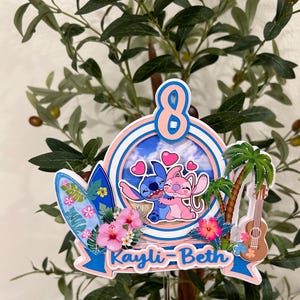 Może przedstawiać: Kolorowy topper na tort o tematyce tropikalnej z cyfrą 8. Zawiera deskę surfingową, palmę, ukulele i imię "Kayli-Beth". Projekt przedstawia postacie z kresk&oacute;wek obejmujące się, otoczone sercami i kwiatami.
