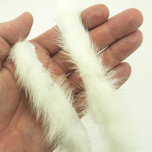 May include: Two strands of white rabbit fur, held in a hand, for use in fly tying or other craft projects.