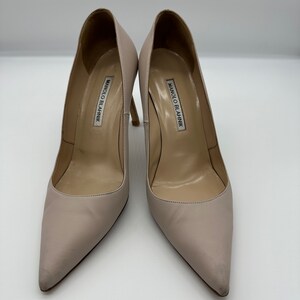 May include: A pair of light beige Manolo Blahnik high heels. The shoes have pointed toes and stiletto heels. The brand name is printed on the insole of each shoe. The heels are approximately 4 inches tall.
