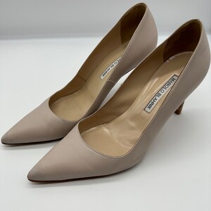 May include: A pair of light beige Manolo Blahnik pumps. The shoes have pointed toes and stiletto heels. The brand name is printed on the insole. The pumps are made of a smooth leather-like material.