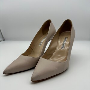 May include: A pair of light beige high-heeled pumps with pointed toes. The shoes have a stiletto heel and a smooth leather finish. The brand name "MANOLO BLAHNIK" is visible on the insole.