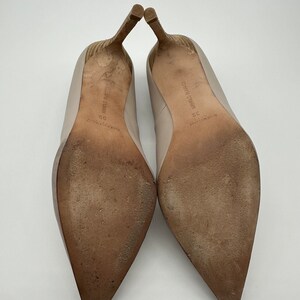 May include: A pair of beige high-heeled shoes with pointed toes, showing the soles. The heels are a light brown color with a textured design. The soles are worn and show signs of use. The shoes are size 39.