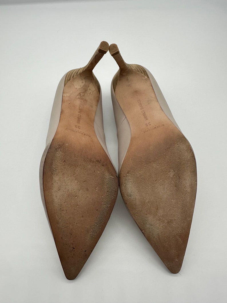 May include: A pair of beige high-heeled shoes with pointed toes, showing the soles. The heels are a light brown color with a textured design. The soles are worn and show signs of use. The shoes are size 39.