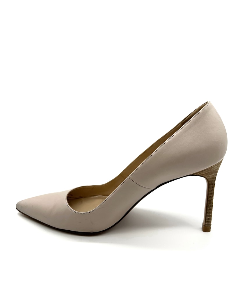 May include: A light beige pointed-toe pump with a stiletto heel. The heel has a wood-grain pattern. The shoe has a low-cut vamp and a smooth, solid color upper. The shoe is set against a white background.