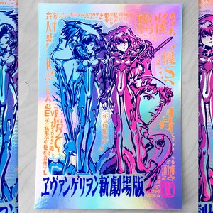 May include: A holographic poster with a blue, pink, and purple color scheme. The poster features a group of anime characters with the text "Evangelion: New Theatrical Edition" in Japanese.