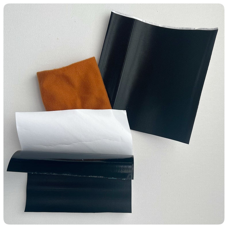May include: Three pieces of black duct tape, one folded in half, one lying flat, and one partially folded over a white piece of paper. A piece of orange fabric is also visible.