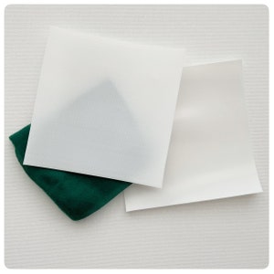 May include: Two white sheets of paper, one on top of the other, with a green fabric underneath. The top sheet of paper is slightly larger than the bottom sheet.