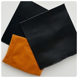May include: Two black fabric squares and one orange fabric square. The black fabric squares have a textured surface. The orange fabric square is smooth.