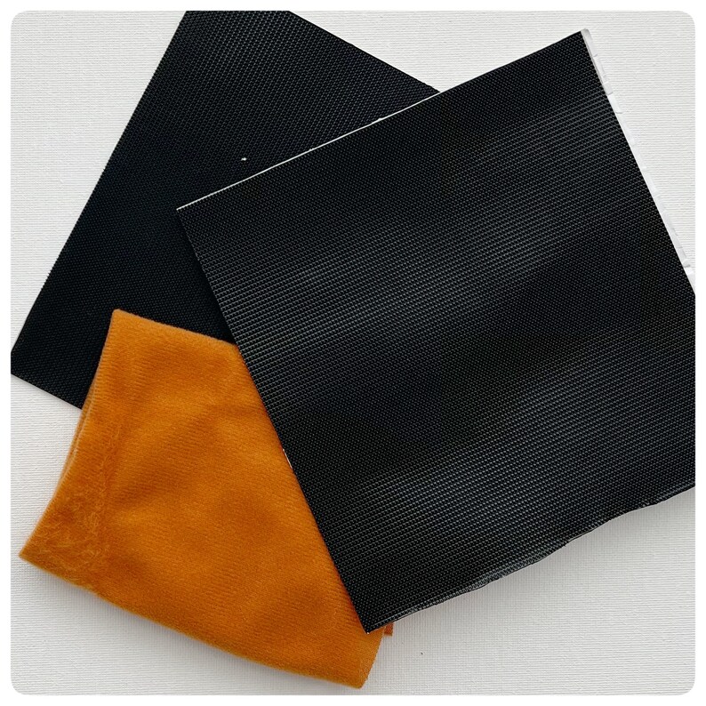 May include: Two black fabric squares and one orange fabric square. The black fabric squares have a textured surface. The orange fabric square is smooth.