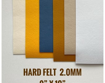 Könnte beinhalten: Eine Sammlung von sechs rechteckigen Bögen aus hartem Filz in Creme, Gelb, Blau, Senf, Beige und Weiß. Der Text HARD FELT 2.0MM 9" X 10" ist unten aufgedruckt. Jeder Bogen hat eine gleichmäßige, dichte Textur und eine flache Oberfläche.