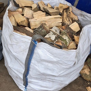May include: A white fabric sack filled with pieces of firewood. The sack has blue and black straps.