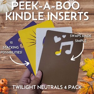 May include: Four Kindle inserts in purple, yellow, silver, and brown are held in a hand. The inserts feature cut-out designs of a musical note and hearts. Text on the inserts reads "PEEK-A-BOO KINDLE INSERTS", "12 STACKING POSSIBILITIES!", "SWAPS MADE SIMPLE", and "TWILIGHT NEUTRALS 4 PACK".