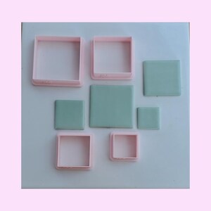 May include: A set of four light pink square cookie cutters of varying sizes arranged alongside four corresponding light green square shapes. The cutters have open centers and raised edges, while the green squares are solid and flat.