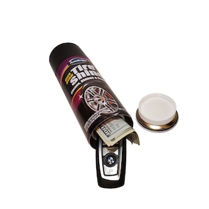 May include: A black can with a label that says "AutoBright One Step Tire Shine" and a picture of a tyre. The can is open and there is cash and a car key inside.