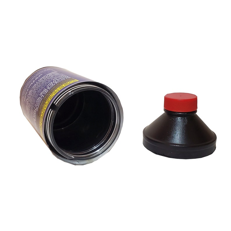 May include: An open black plastic bottle with a red lid. The bottle is empty and the lid is off. The bottle is sitting on a white surface.