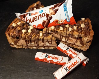 May include: A chocolate cookie crust pie filled with layers of chocolate and hazelnut spread, topped with chocolate chips and white chocolate chips. Three Kinder Bueno chocolate bars are in the foreground, two of which are unwrapped.