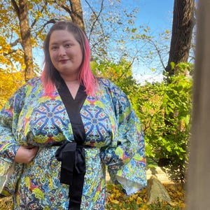 May include: A colorful kimono with a vibrant pattern of blue, green, and yellow designs. The kimono has a black satin trim and a matching tie belt. The sleeves are wide and flowing, and the overall style is relaxed and comfortable.