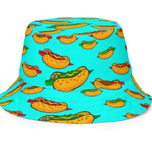 May include: A turquoise bucket hat featuring a repeating pattern of cartoon hot dogs. The hot dogs have various toppings, including ketchup, mustard, and a crocodile-shaped hot dog. The hat is a fun and playful accessory.