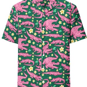 May include: Short-sleeved button-down shirt with a green background and a repeating pattern of pink alligators and white and yellow flowers. The shirt has a classic collar and white buttons.