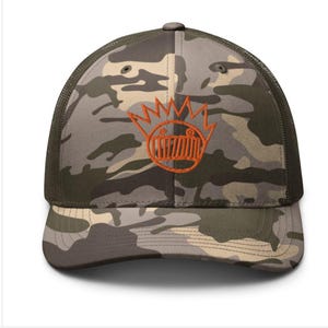 May include: A camouflage trucker hat with an orange embroidered graphic of a cartoon face with a crown on top.
