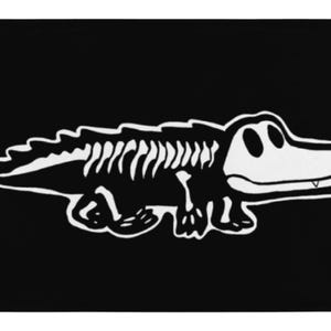 May include: Black flag featuring a white cartoon alligator skeleton design. The alligator is depicted in a simplified, outlined style, with visible ribs and a smiling face. The flag has grommets in the corners.