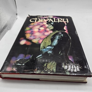 May include: A hardcover book titled "The Age of Chivalry" by the National Geographic Society. The cover features a knight in armor against a dark background with colorful bokeh lights. The book has a red spine.