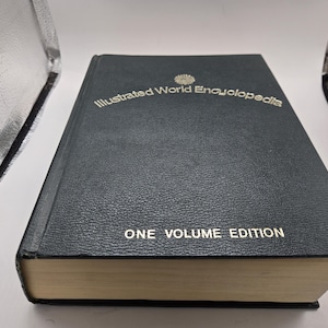 May include: A dark green, hardcover "Illustrated World Encyclopedia" book. The title and "One Volume Edition" are in gold lettering. The book has a textured cover and gold-colored page edges.