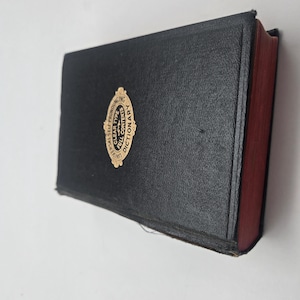 Puede incluir: Un diccionario negro con letras doradas y un emblema dorado en la portada. El libro tiene páginas con bordes rojos y el título "Universal Self-Pronouncing Dictionary" es visible. El libro está cerrado y parece estar en buenas condiciones.