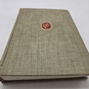 Op de afbeelding: Een groen linnen gebonden hardcover boek met een gouden en rood rond embleem op de voorkant.