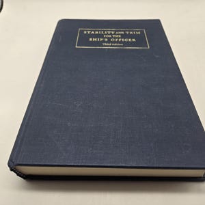 May include: A navy blue hardcover book with the title "Stability and Trim for the Ship's Officer" in gold lettering on the front cover. The book is the third edition.