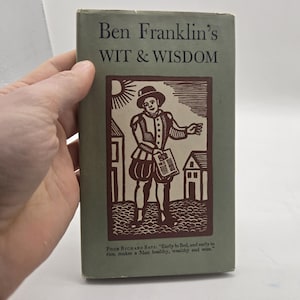 May include: A vintage book titled "Ben Franklin's WIT & WISDOM" with a green cover. The cover features a brown illustration of a man in historical attire, holding a paper. The text "Poor Richard Says: Early to Bed, and early to rise, makes a Man healthy, wealthy and wise." is printed at the bottom.