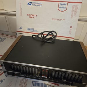 May include: A black and silver Soundcraftsmen audio frequency equalizer with wooden side panels. The device features two channels, labeled Channel A and Channel B, each with multiple vertical sliding faders for sound adjustment and a black power cord.