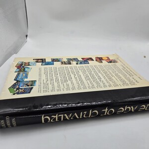 May include: A hardcover book titled "The Age of Chivalry" by the National Geographic Society. The book has a black spine with white text and a colorful cover featuring various images. The book is lying on a white surface.
