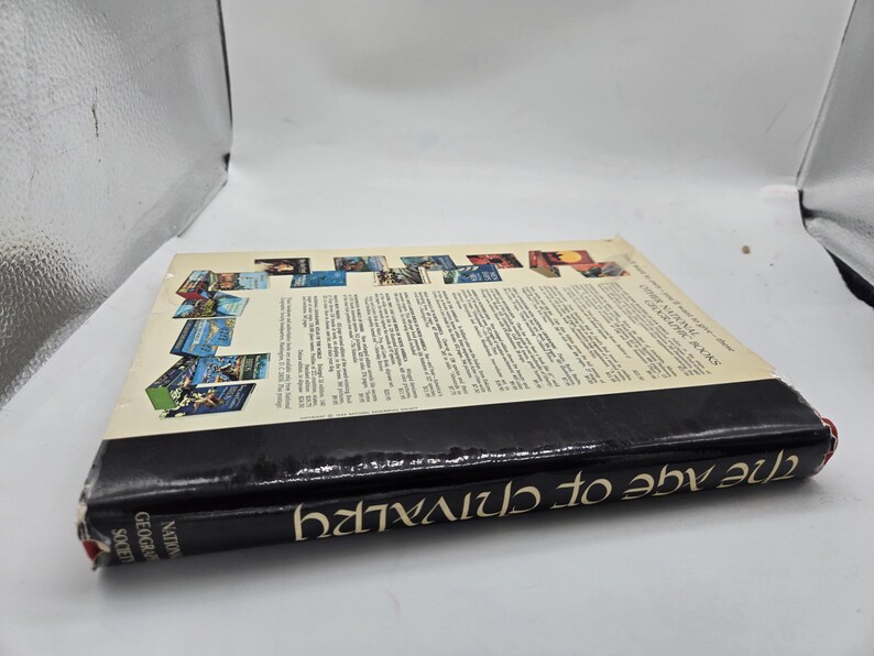 May include: A hardcover book titled "The Age of Chivalry" by the National Geographic Society. The book has a black spine with white text and a colorful cover featuring various images. The book is lying on a white surface.