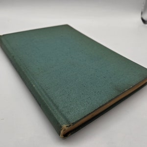 Peut inclure: Un livre relié vert avec une couverture texturée. Le livre est fermé et posé sur une surface blanche.