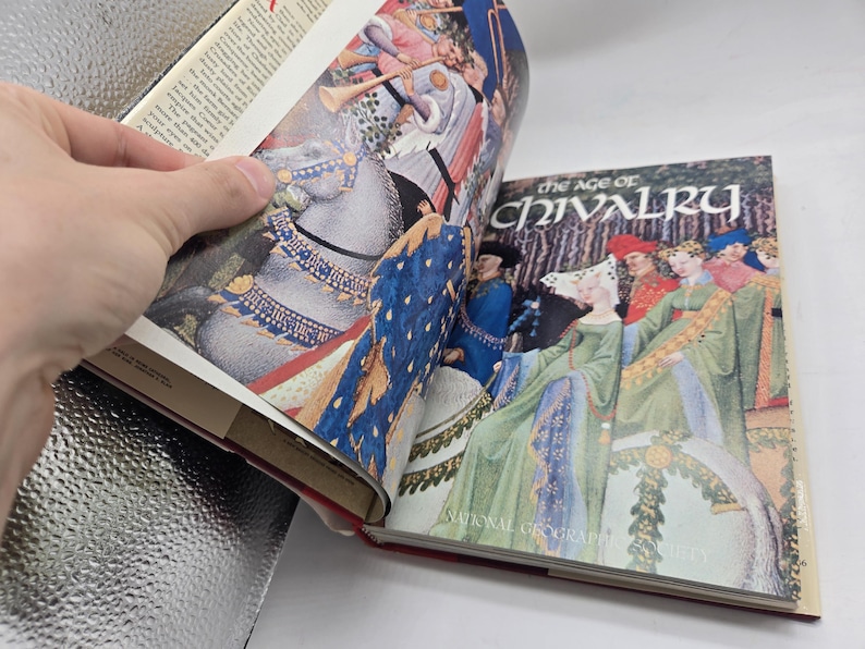 May include: Open book with colorful illustrations. One page shows a knight on a horse, the other displays a group of people in medieval attire. The book's cover reads "The Age of Chivalry" by National Geographic Society.