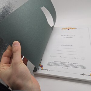 May include: A book with a dark green cover being opened to reveal white pages with text. The title "The New World Book Of Anderson" is visible. The book is published by Walter's Family Heritage.