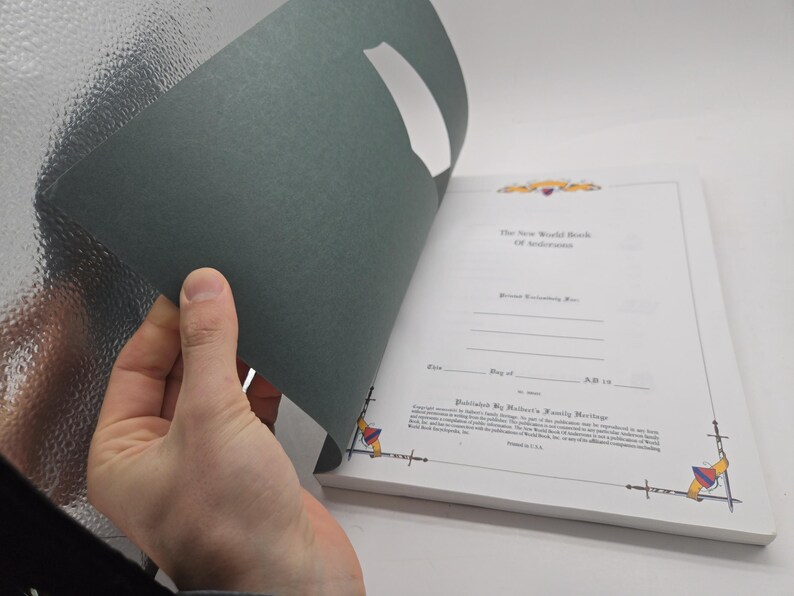 May include: A book with a dark green cover being opened to reveal white pages with text. The title "The New World Book Of Anderson" is visible. The book is published by Walter's Family Heritage.