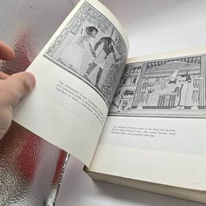Puede incluir: Un libro abierto con ilustraciones en blanco y negro de arte egipcio antiguo. Las p&aacute;ginas se mantienen abiertas, revelando dibujos detallados de figuras y jerogl&iacute;ficos. Las p&aacute;ginas del libro son de color blanquecino.