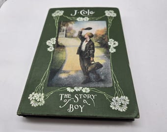 May include: A vintage book titled "The Story of Boy" by J. Cole. The cover is dark green with white floral accents and a central illustration of a boy on a path. The boy is holding a briefcase and waving a hat.