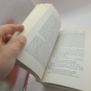 Puede incluir: Un libro abierto con p&aacute;ginas blanquecinas, sostenido por una mano. El texto est&aacute; en ingl&eacute;s, con t&iacute;tulos y p&aacute;rrafos visibles. Las p&aacute;ginas del libro est&aacute;n ligeramente amarillentas. El fondo es una superficie clara y reflectante.
