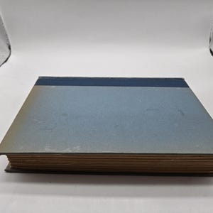 May include: A blue hardcover book with a dark blue band around the spine. The book is closed and sitting on a white surface.