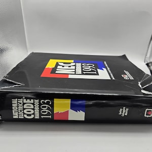 Könnte beinhalten: Ein schwarzes National Electrical Code Handbook 1993. Das Buch hat ein farbenfrohes Logo mit den Buchstaben "NEC" und dem Jahr 1993. Der Buchrücken trägt den Titel "National Electrical Code Handbook 1993" in weißem Text.