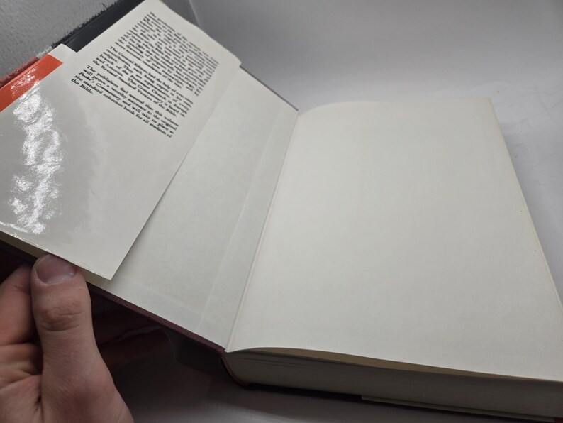 May include: A closed hardcover book with a white cover and a red spine. The book has a glossy cover and a small amount of text on the spine.