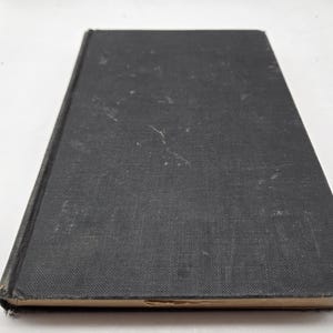 May include: A black hardback book with a worn, textured cover. The book is closed and lying flat on a white surface.